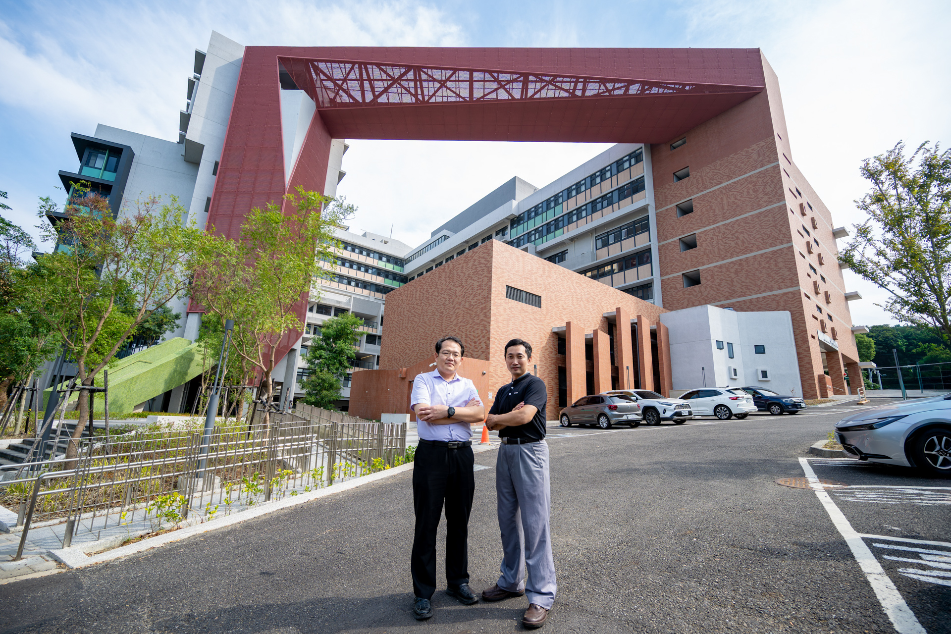 Dean Tzu-Hua Wang (left) and Associate Dean Chun-Min Wang in front of the new building. The red beam behind them symbolizes the “Gate of Virtue,” representing the passing down of educational values.